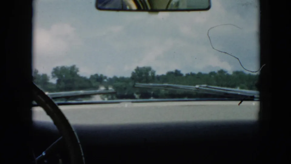 1956 Cuba travel footage shows the car dashboard and wipers facing outward toward water, trees, and a low shoreline from the ferry.