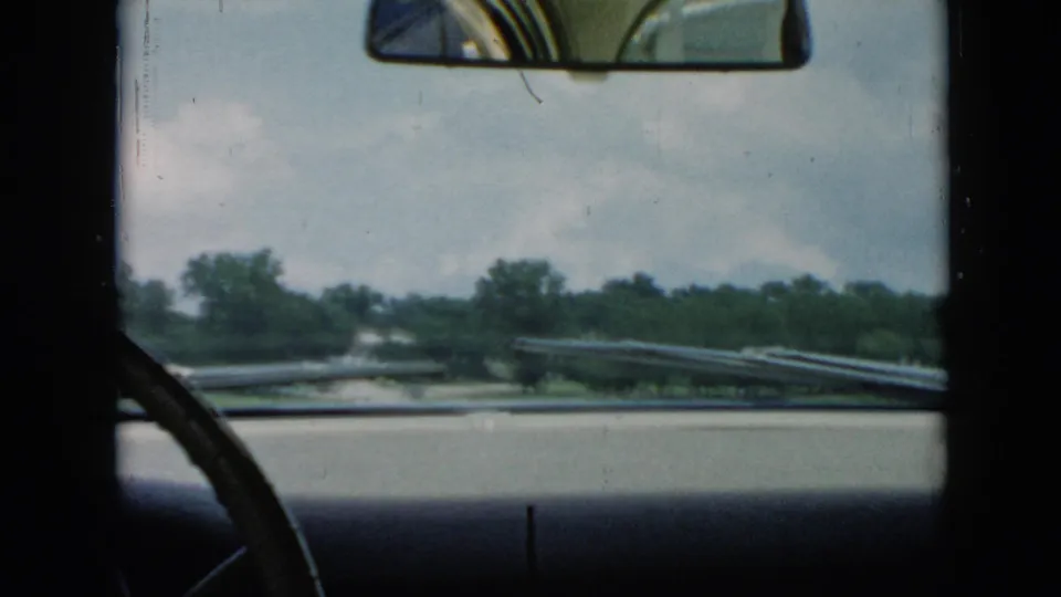 The final 1956 Cuba frame holds on the car windshield, rearview mirror, wipers, water, and tree-lined shore beyond the ferry.