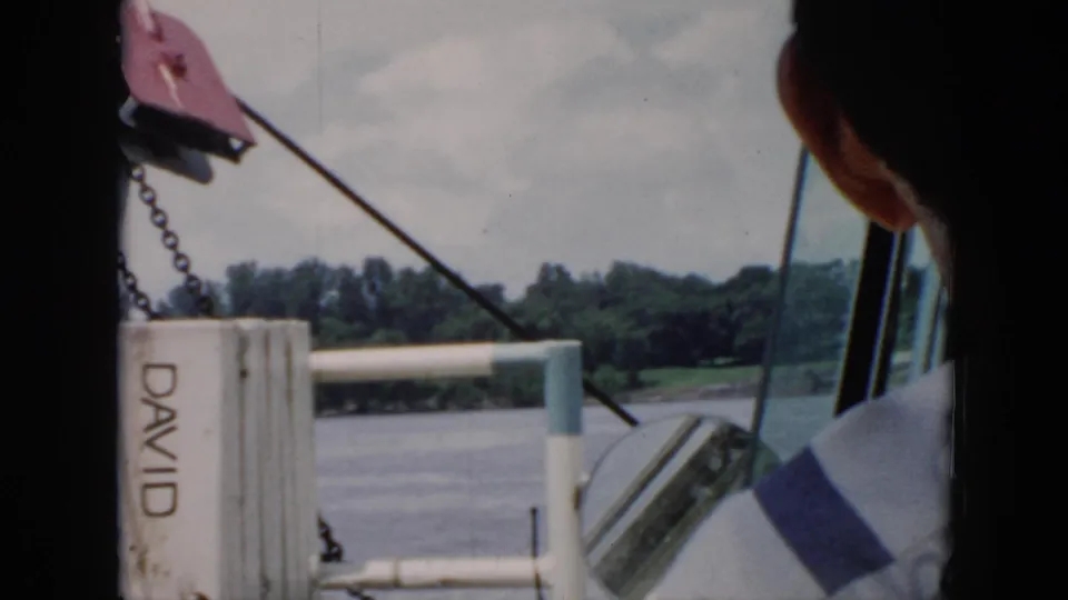 1956 Cuba boating frame showing lake water, white railings, a post marked DAVID, and an adult partly seen from behind.