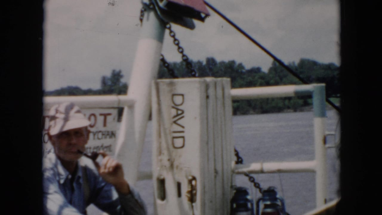 Man holds a pipe near his mouth on a boat with water behind him.