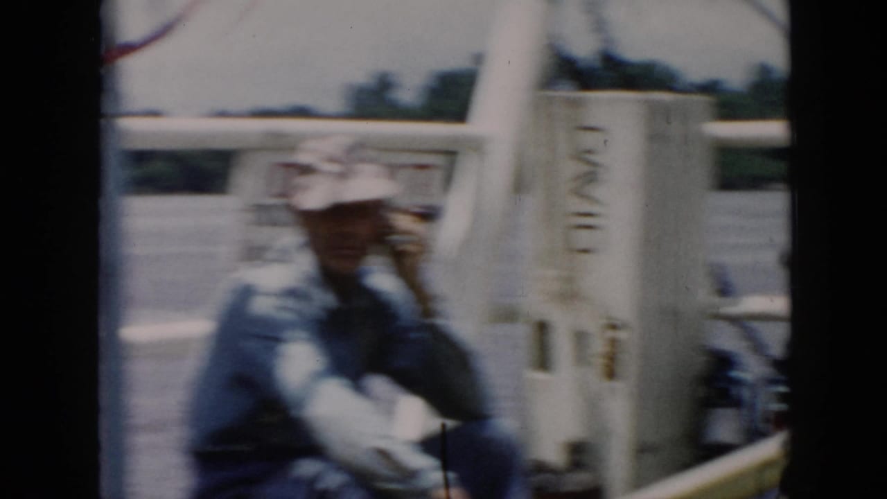 1956 8mm home-movie frame identified as Cuba, showing a man on a boat holding a handheld radio-like device near white railings.