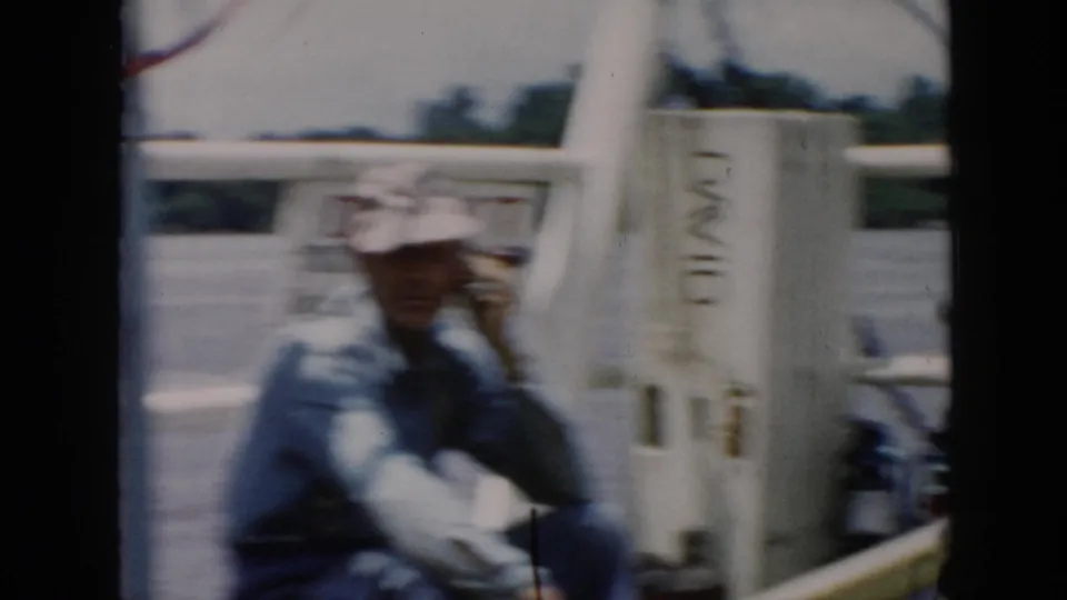 1956 8mm home-movie frame identified as Cuba, showing a man on a boat holding a handheld radio-like device near white railings.