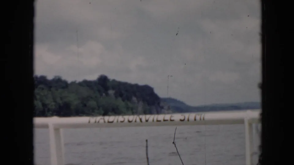 1956 8mm home-movie frame identified as Cuba, looking from a boat past Madisonville lettering toward water and a wooded shore.