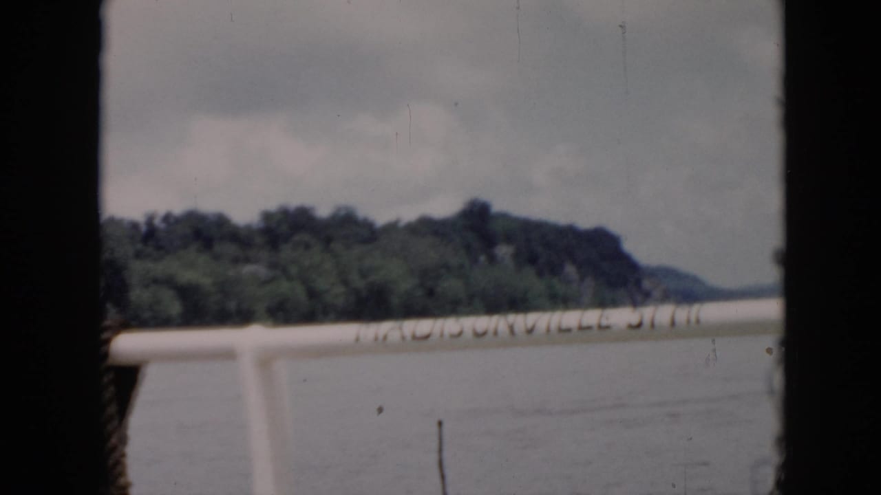 1956 Cuba home-movie frame from a boat, showing railing text over water with trees and shoreline in the distance.
