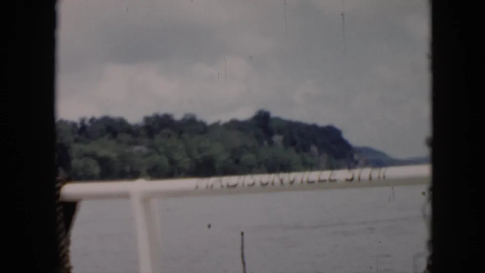 1956 Cuba home-movie frame from a boat, showing railing text over water with trees and shoreline in the distance.