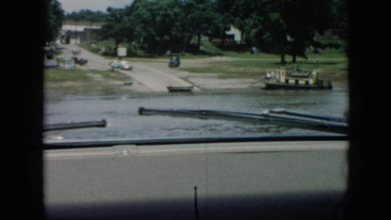 Waterfront landing with road, trees, small dock, cars, and a small boat.