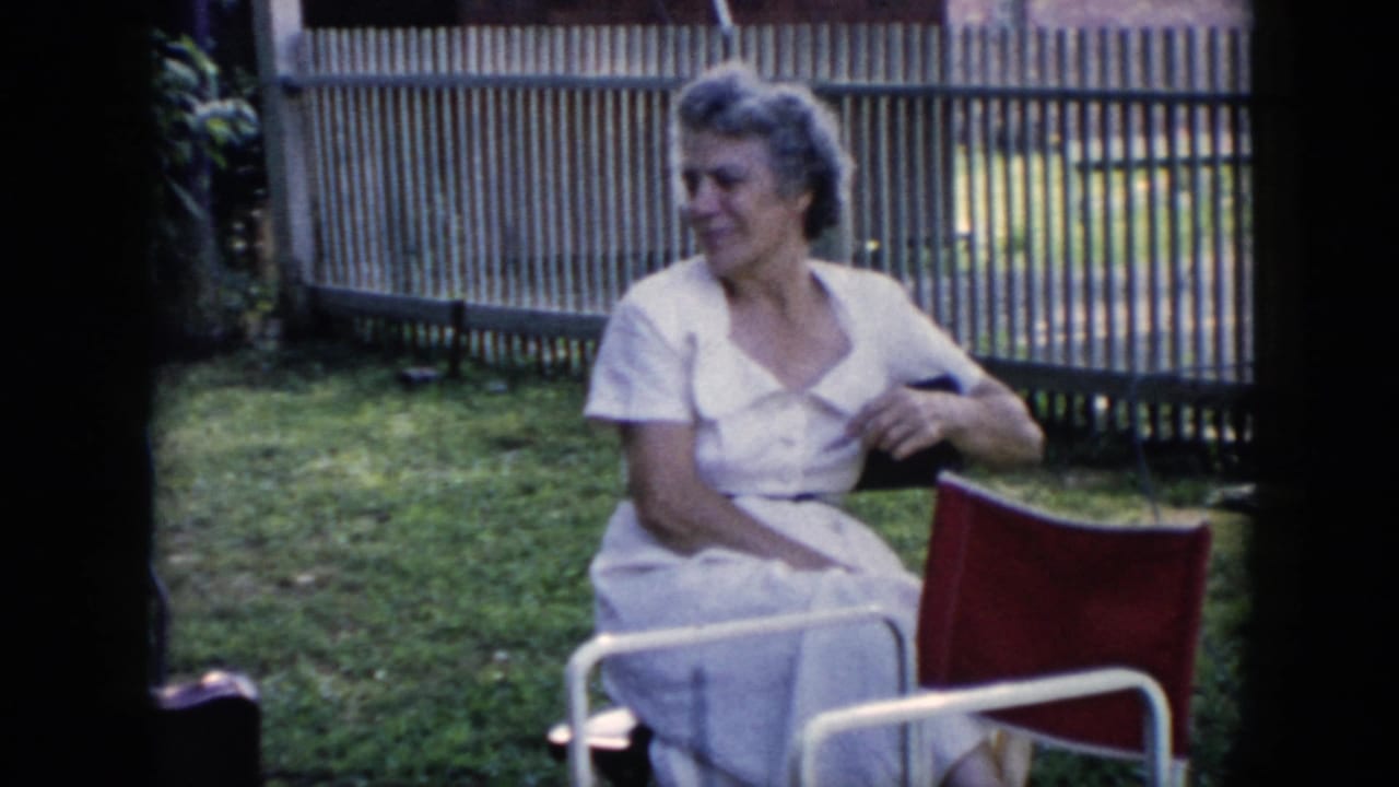 Woman in a white dress sits in a red chair and turns her head in the yard.