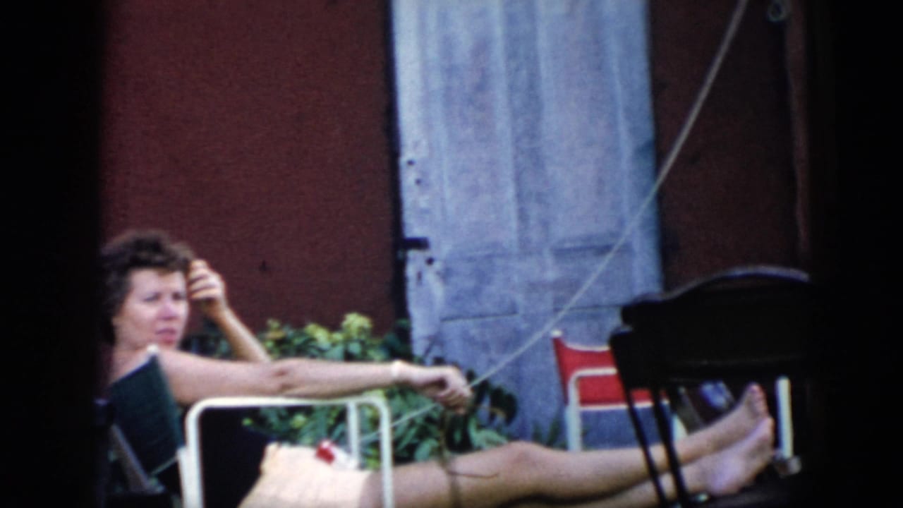 A woman lounges in a folding chair in a Cuba backyard setting, with red wall, blue shutters, greenery, and a dark chair nearby.