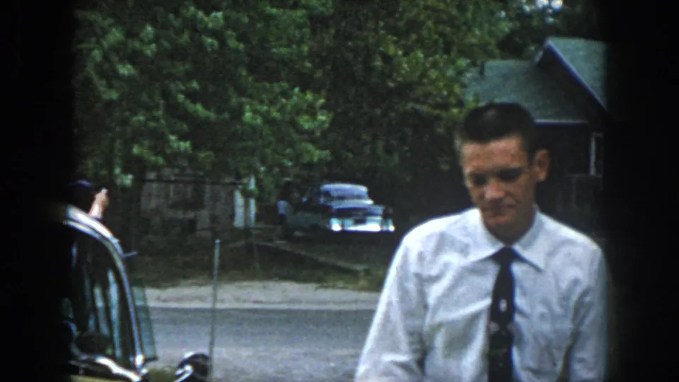 The man appears closer to the camera in the final frame, with the car edge, road, trees, and residential background still visible.