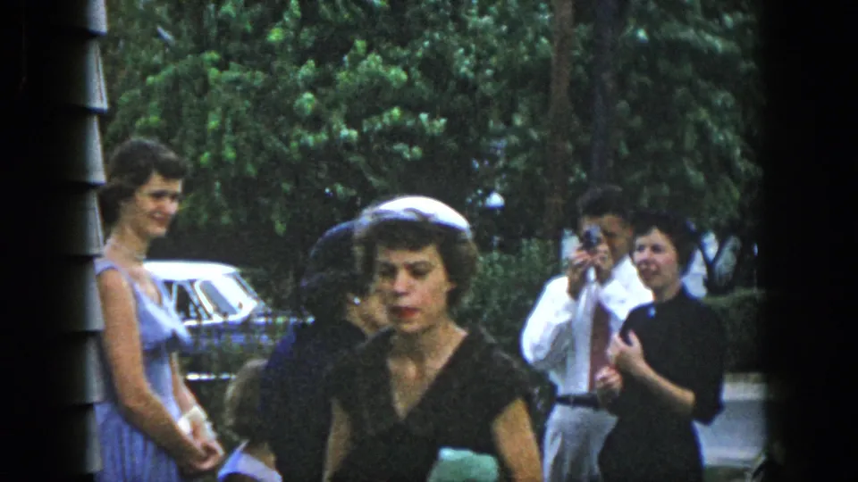 Dayton, Ohio 1958 frame showing several adults outdoors, including women in dark dresses, a woman in blue, and a man holding a camera.