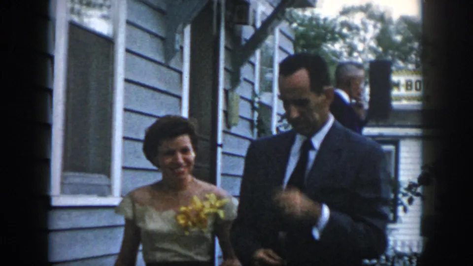 1958 Dayton frame showing a smiling woman in a light dress with corsage beside a suited man outside a clapboard house.