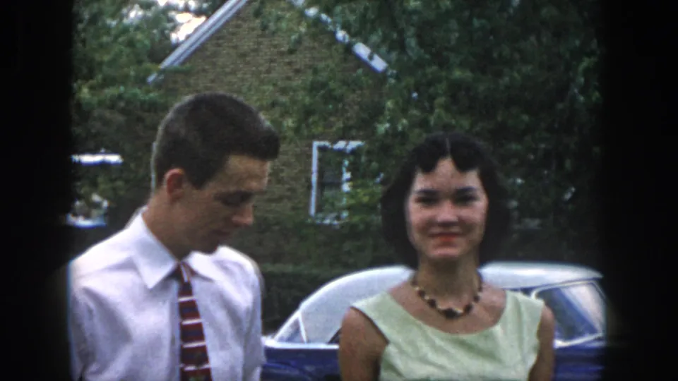 A young man in a white shirt and striped tie stands beside a young woman in a pale green dress near a parked car in Dayton, Ohio.