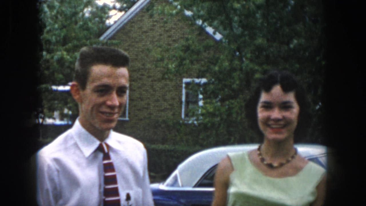 In Dayton, Ohio 1958 home-movie footage, a young couple stands outside by a blue classic car and brick house.