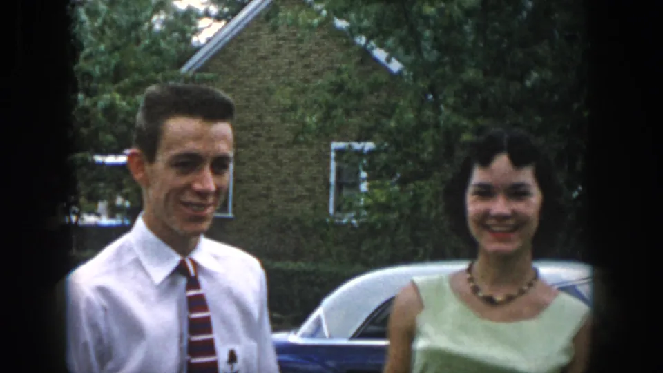 In Dayton, Ohio 1958 home-movie footage, a young couple stands outside by a blue classic car and brick house.