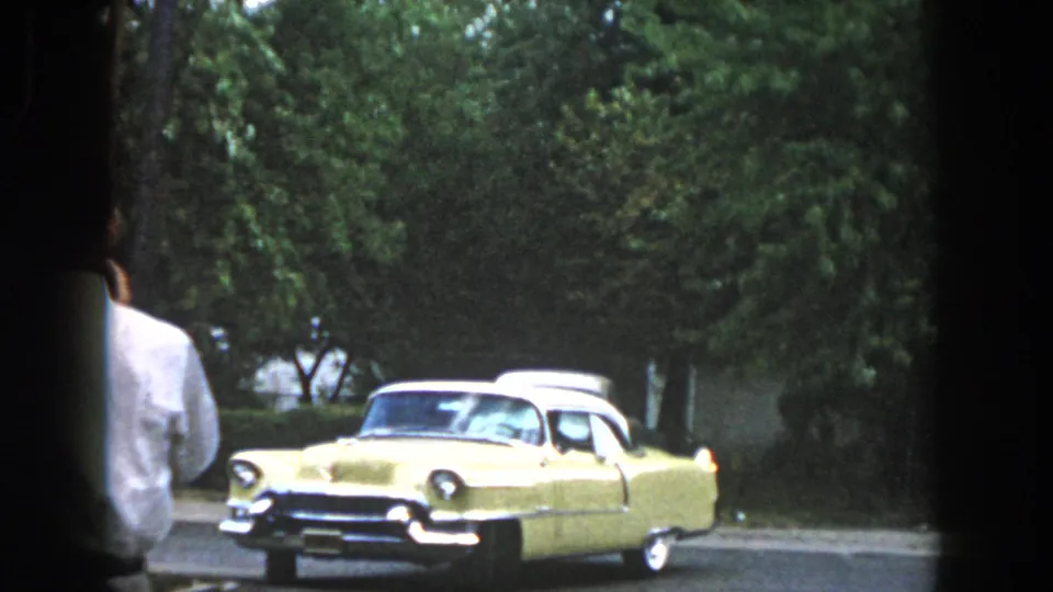 Dayton, Ohio 1958 home-movie view of a pale yellow 1950s car near a casually framed adult figure and roadside trees.