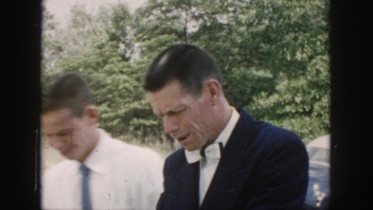 Two men in formal wedding clothing stand outdoors in Dayton, with one wearing a dark suit and bow tie and another in a white shirt and tie.