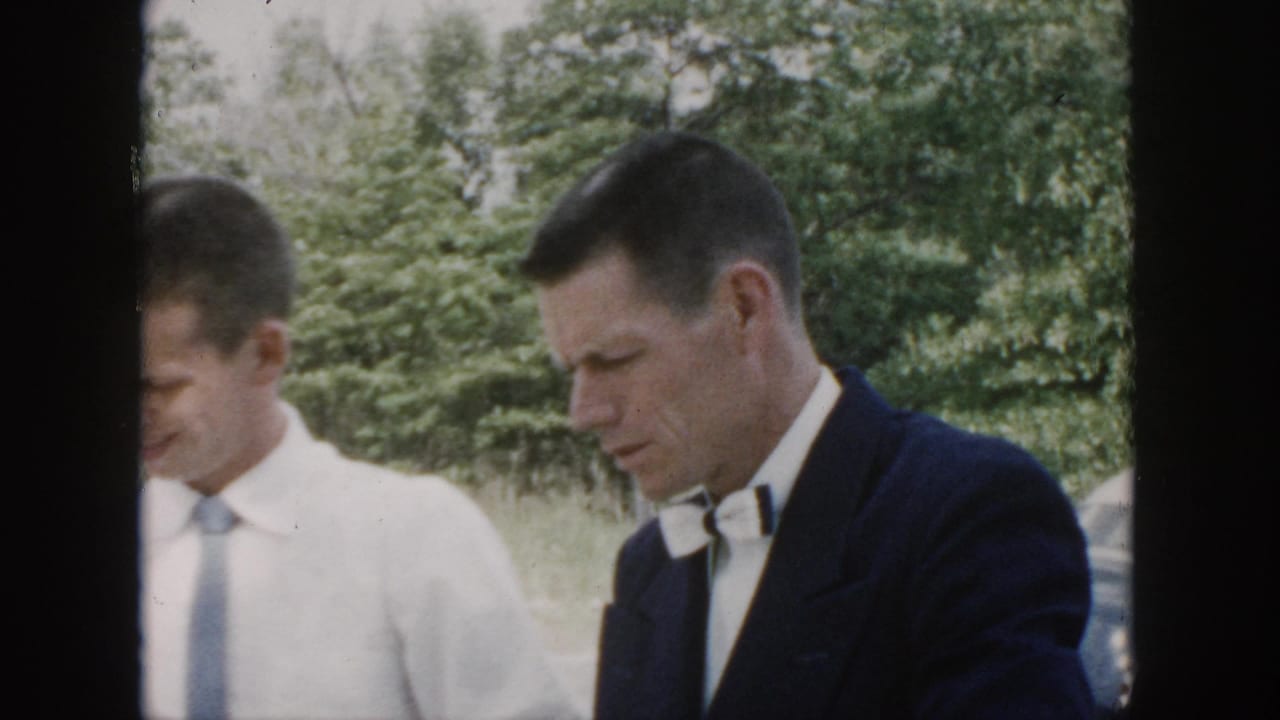 The outdoor wedding scene continues with two men in formal attire near trees, with a partial car visible at the edge of the frame.