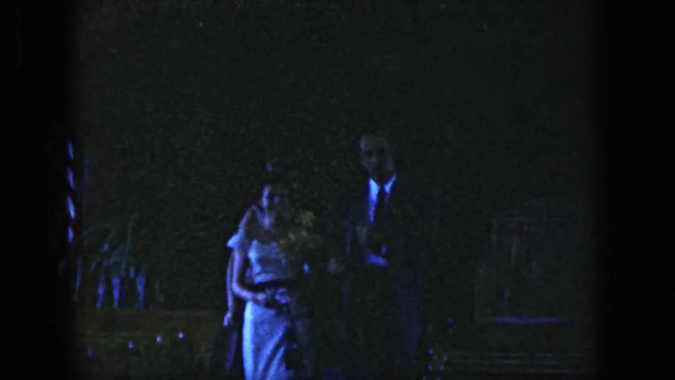 A young couple appears close together in the Dayton 1958 nighttime party footage, framed in soft, grainy low light.