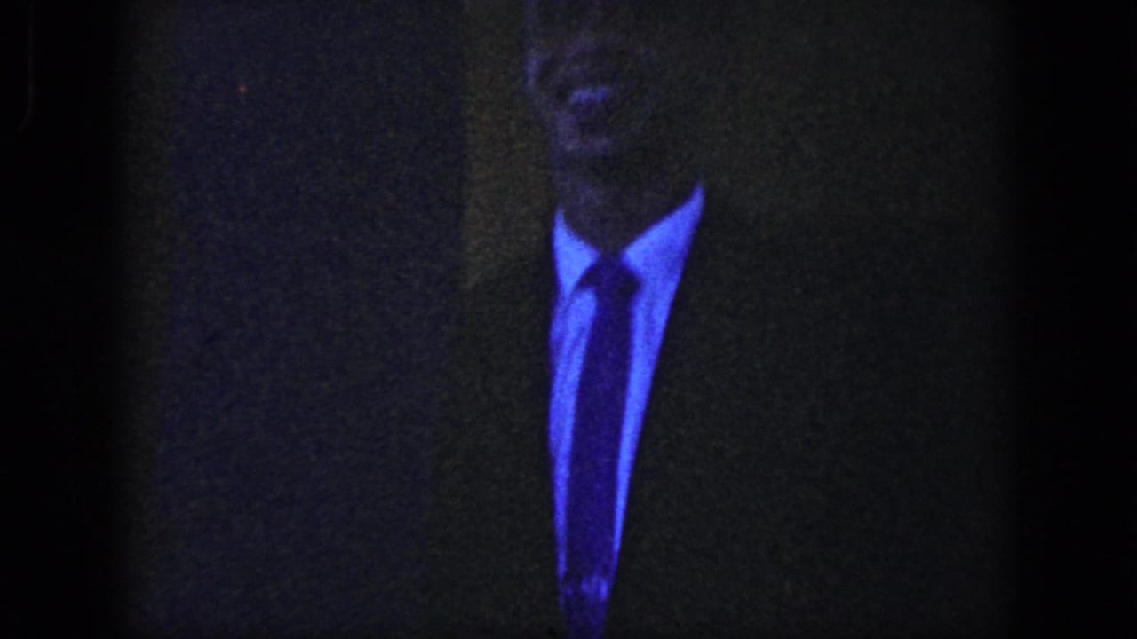 Dark 8mm frame from the wedding sequence showing a suited man in low light before the church exit becomes visible.