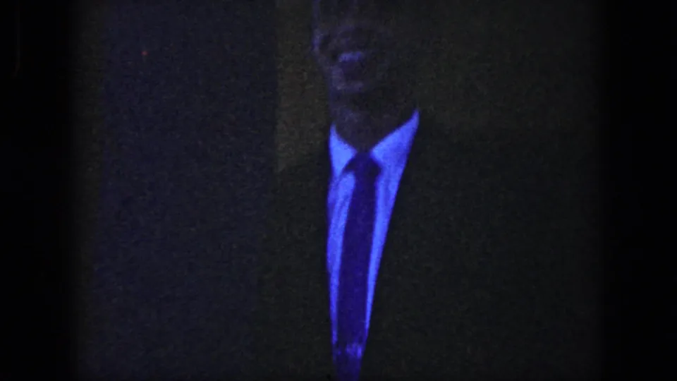 Dark 8mm frame from the wedding sequence showing a suited man in low light before the church exit becomes visible.