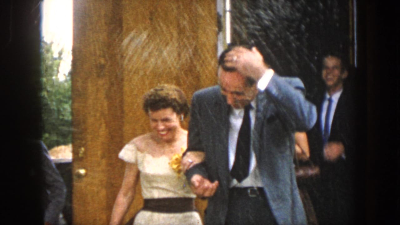 Bride and groom step through a doorway with guests nearby.