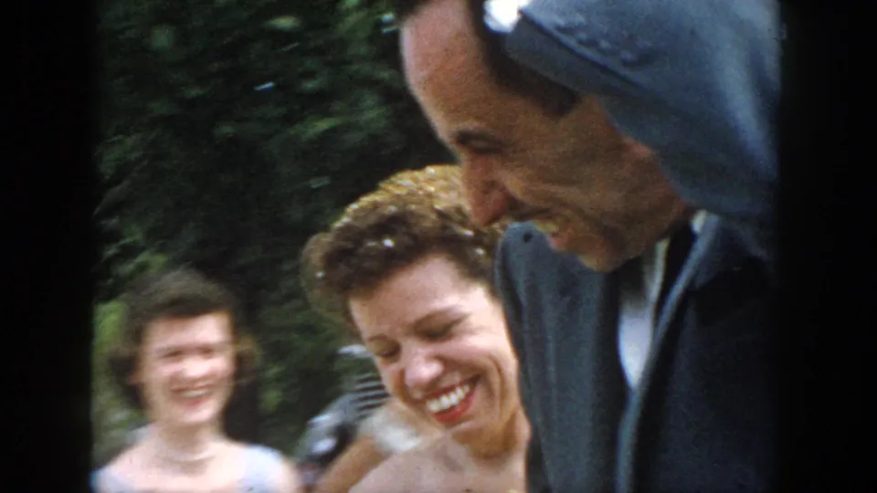 The Dayton wedding couple laughs outdoors in soft motion blur, with greenery and guests visible behind them in the 8mm frame.