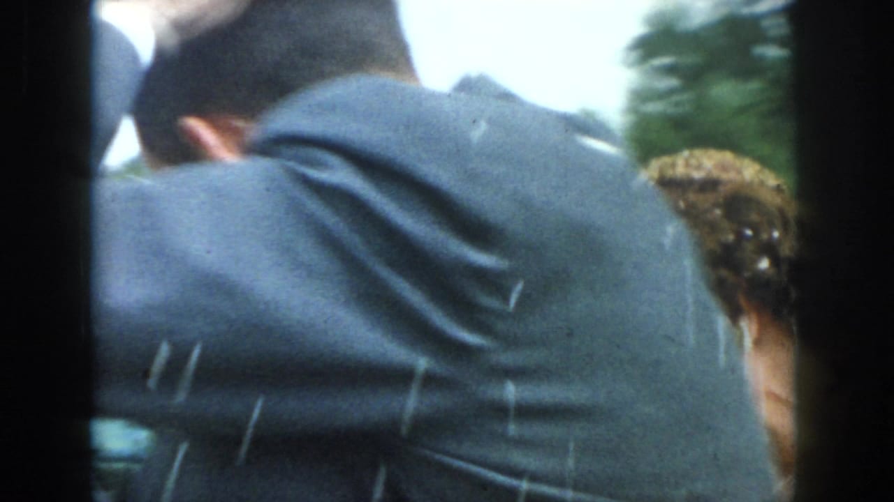 1958 Dayton home-movie frame showing a close, partially obstructed view of suited figures and a bride's headpiece from inside a car.