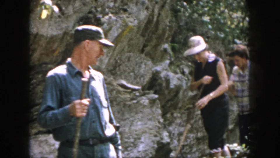 Adults with hats and walking sticks navigate a rocky wooded trail in 1958 Dayton home-movie footage.