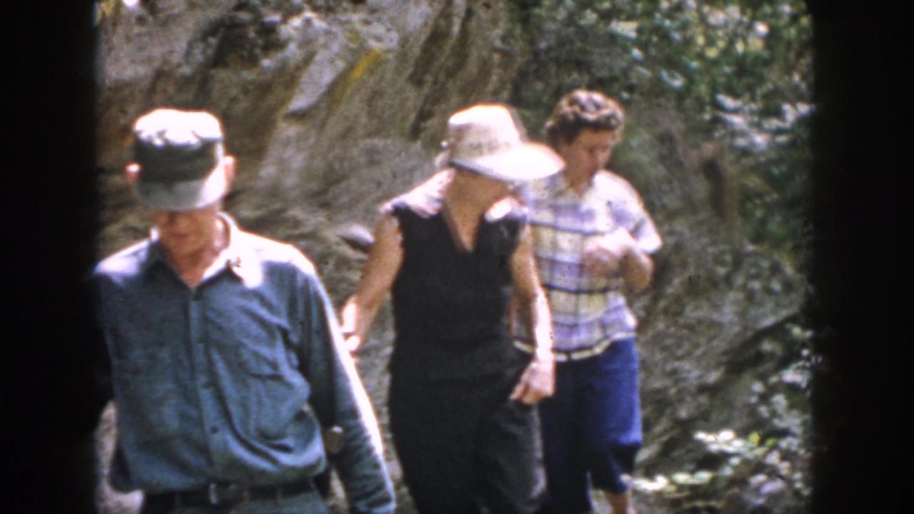 Older hikers in caps and a wide-brimmed hat continue across rocks in the wooded 1958 Dayton, Ohio home movie.