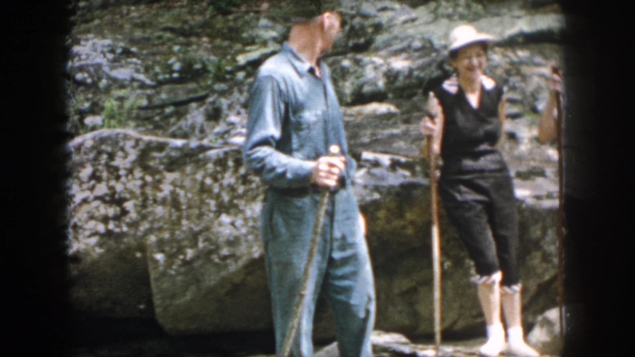A man and woman with walking sticks stand beside layered rocks outdoors.