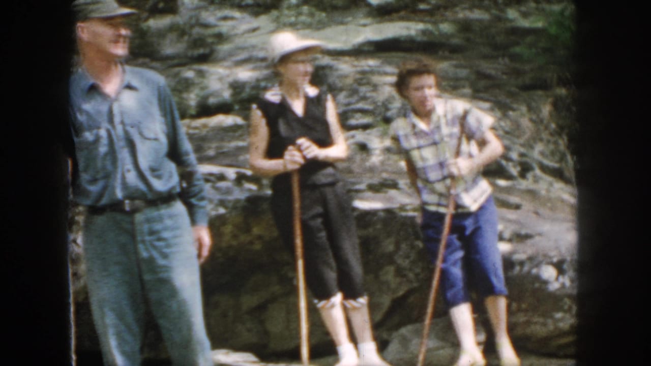 In metadata-supported 1958 Dayton, Ohio footage, three adult hikers pause on rocky terrain with walking sticks near a stream.