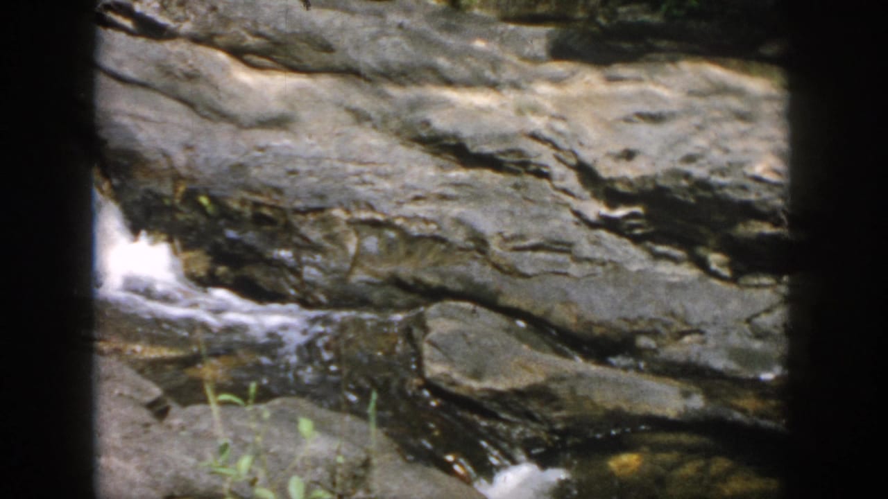 Rocky stream bed with water flowing through layered stone and a small bright cascade.