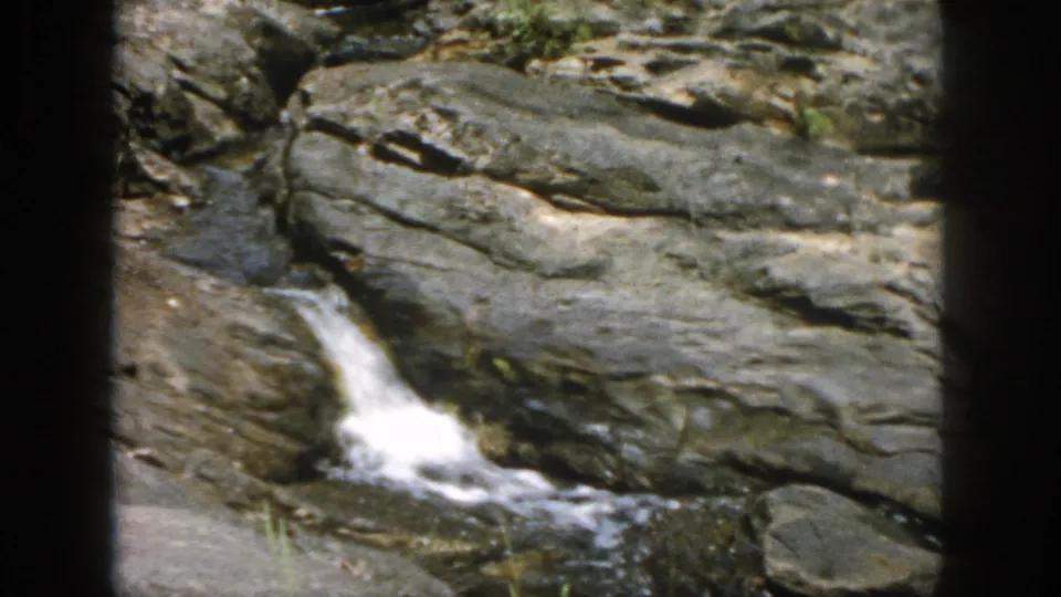 A small waterfall flows over dark rock ledges in the 1958 Dayton, Ohio hiking footage.