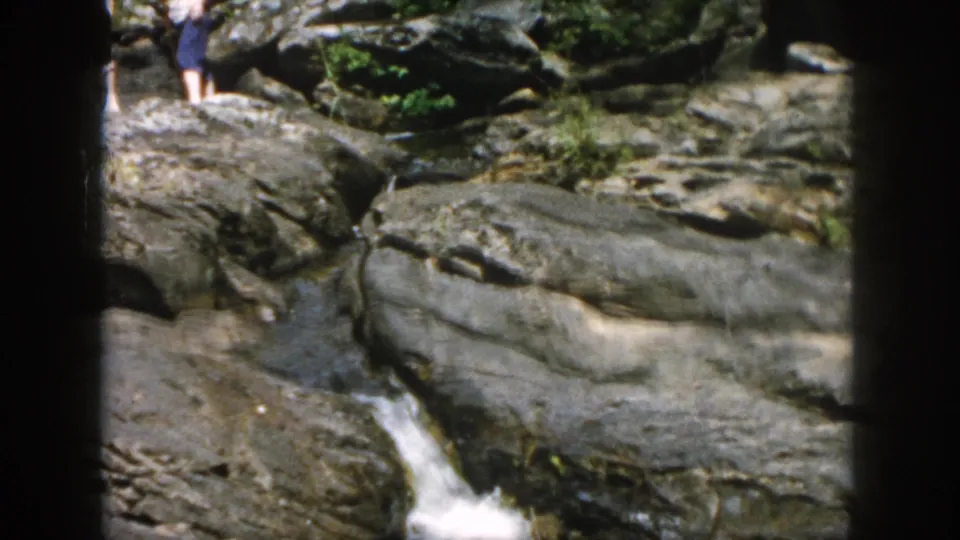 The camera frames a rocky stream and small waterfall, with part of a hiker visible near the top edge of the 1958 scene.