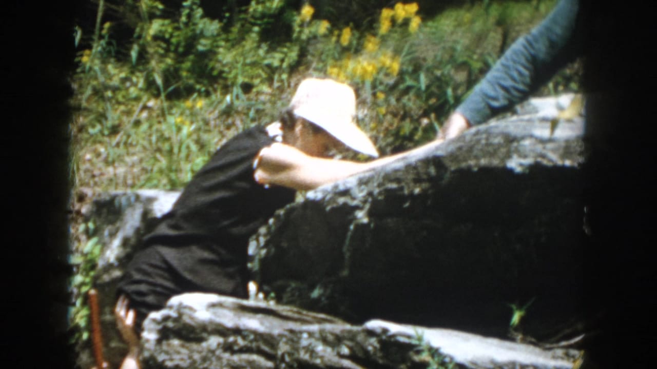 In 1958 Dayton-area home-movie footage, a woman in a white sun hat climbs among dark rocks and greenery.