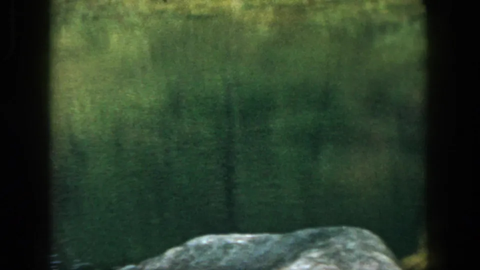 Home-movie view of still green water and a foreground rock during the Dayton, Ohio hiking outing.