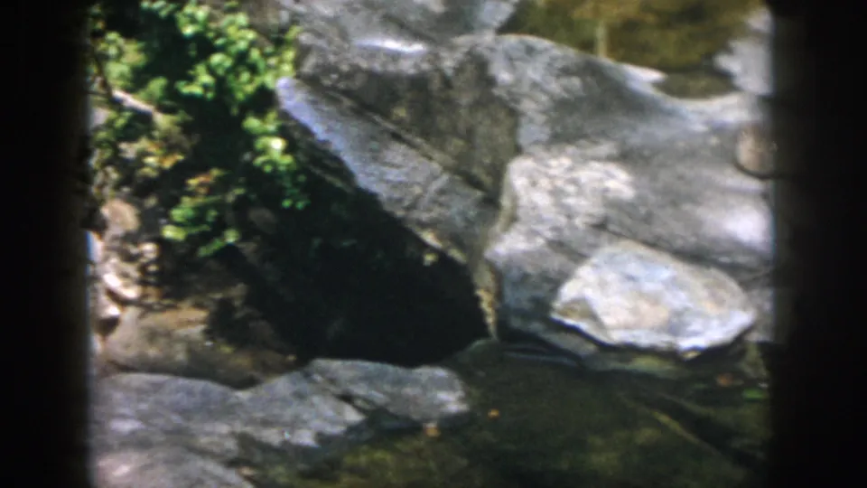 1958 Dayton, Ohio 8mm frame of boulders, small plants, and shallow creek water in a rocky channel.