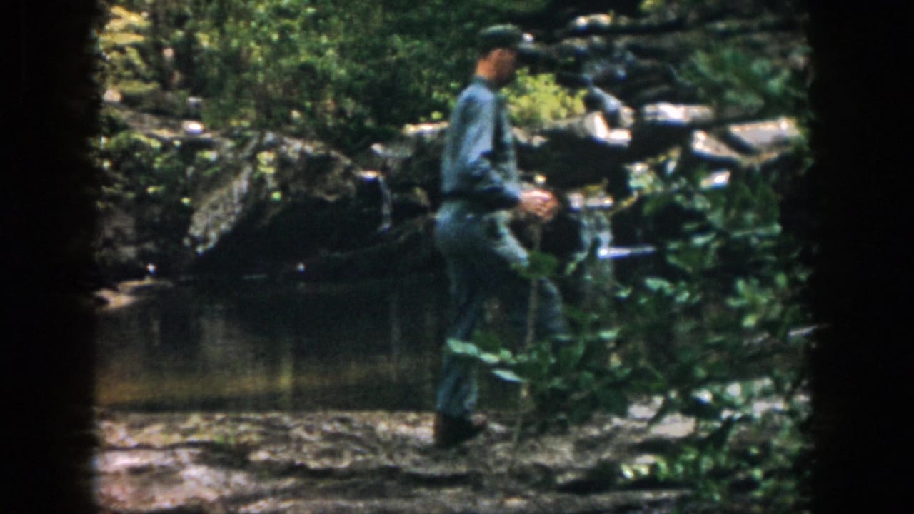 Uniformed man walks along the water's edge with a stick.