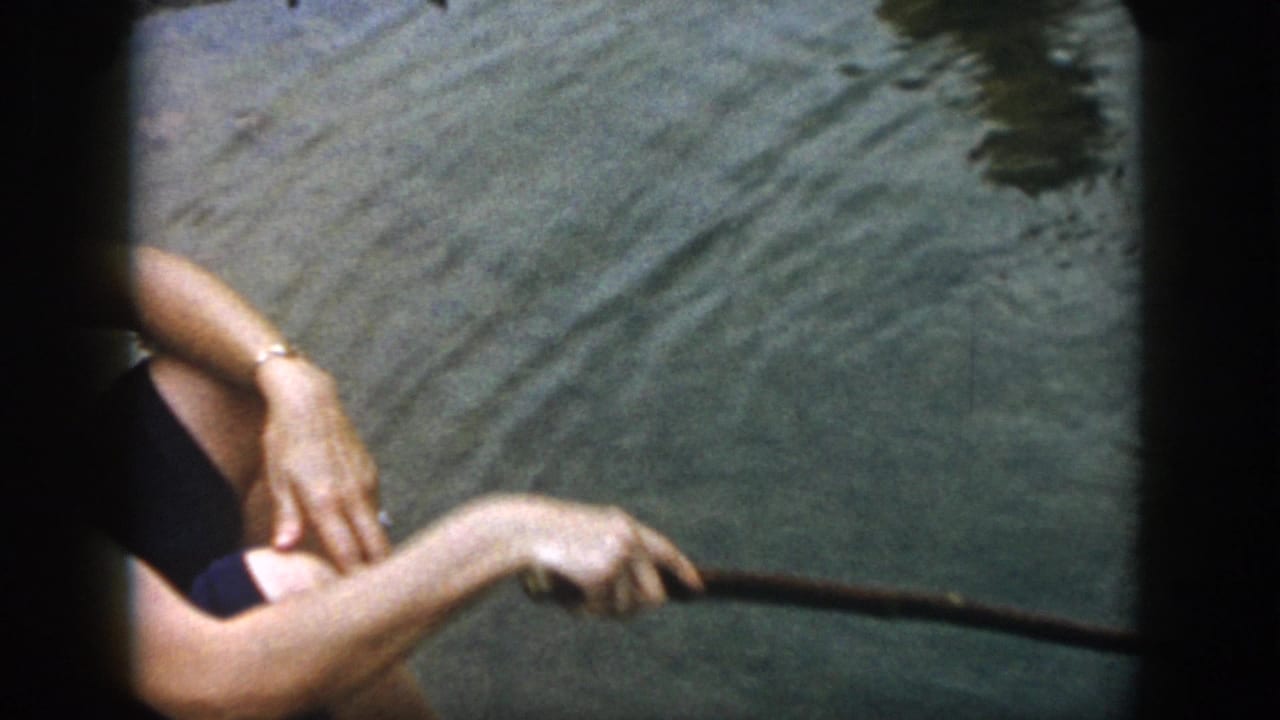 Close view of a person's arm and stick over rippling pond water.