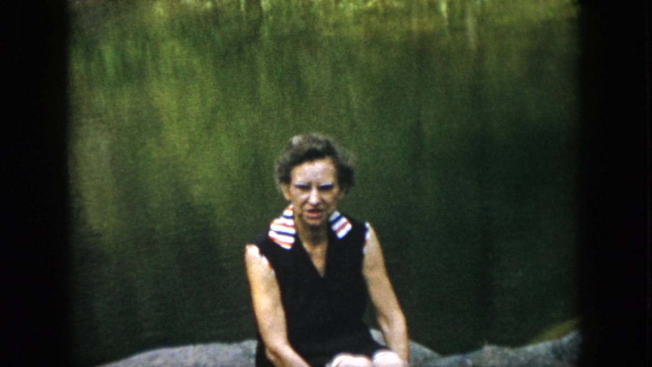 The woman remains seated on the rock, facing the camera in soft 8mm footage from the supplied 1958 Dayton, Ohio setting.