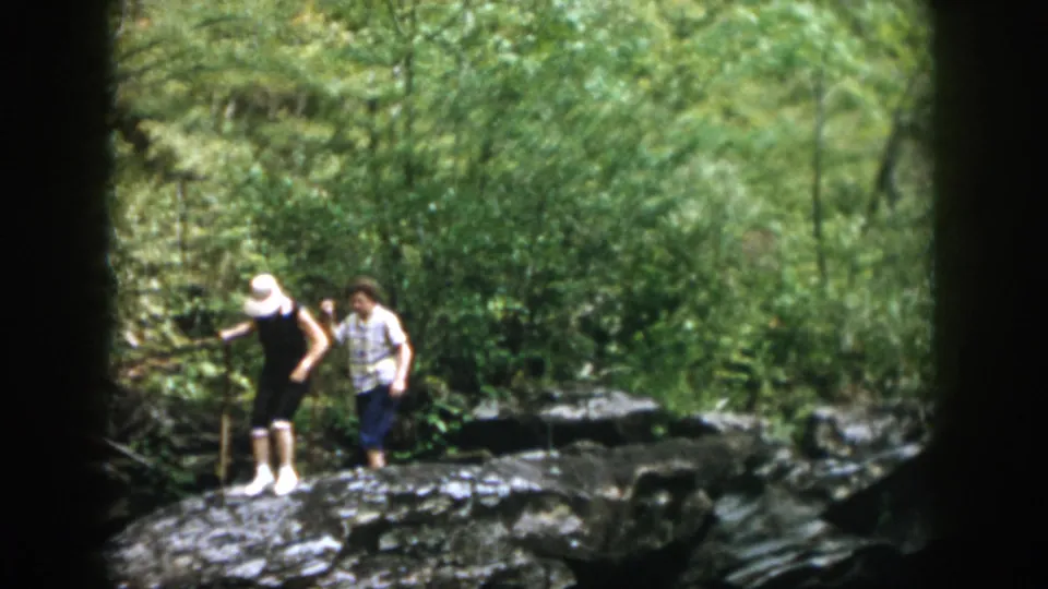 Two people continue across the rocks in the wooded Dayton-area scene, framed by dense summer greenery and soft handheld 8mm motion.