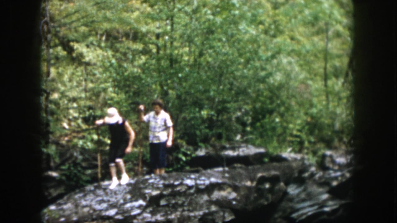 1958 Dayton, Ohio home-movie frame of two adults on a rocky forest trail, with one using a walking stick.