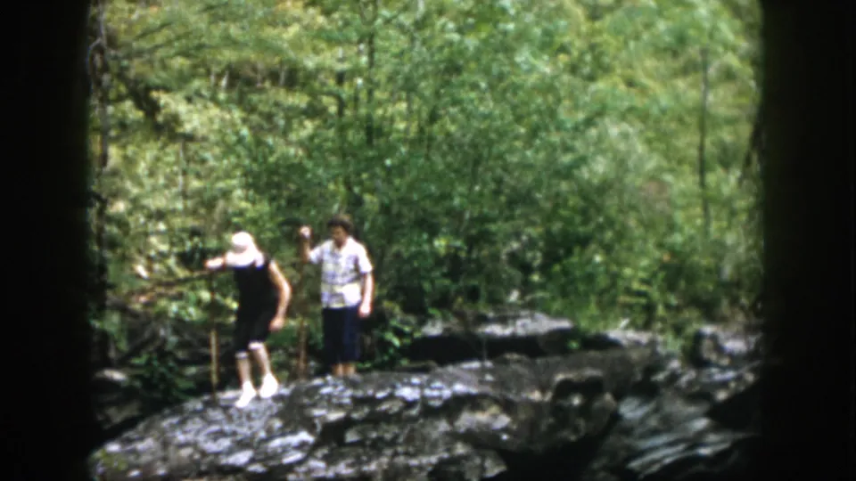 1958 Dayton, Ohio home-movie frame of two adults on a rocky forest trail, with one using a walking stick.