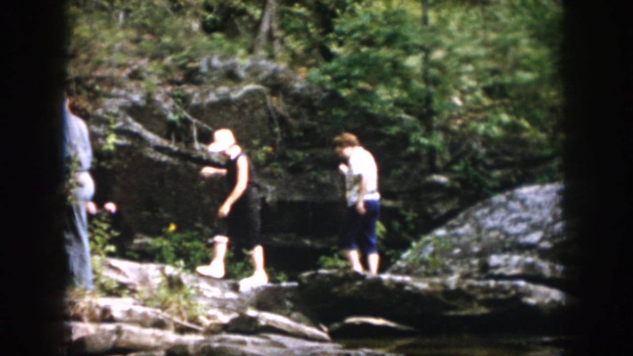 1958 Dayton, Ohio home-movie frame of family members moving carefully over rocks near a wooded stream.