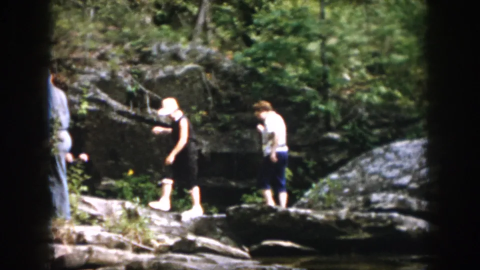 1958 Dayton, Ohio home-movie frame of family members moving carefully over rocks near a wooded stream.
