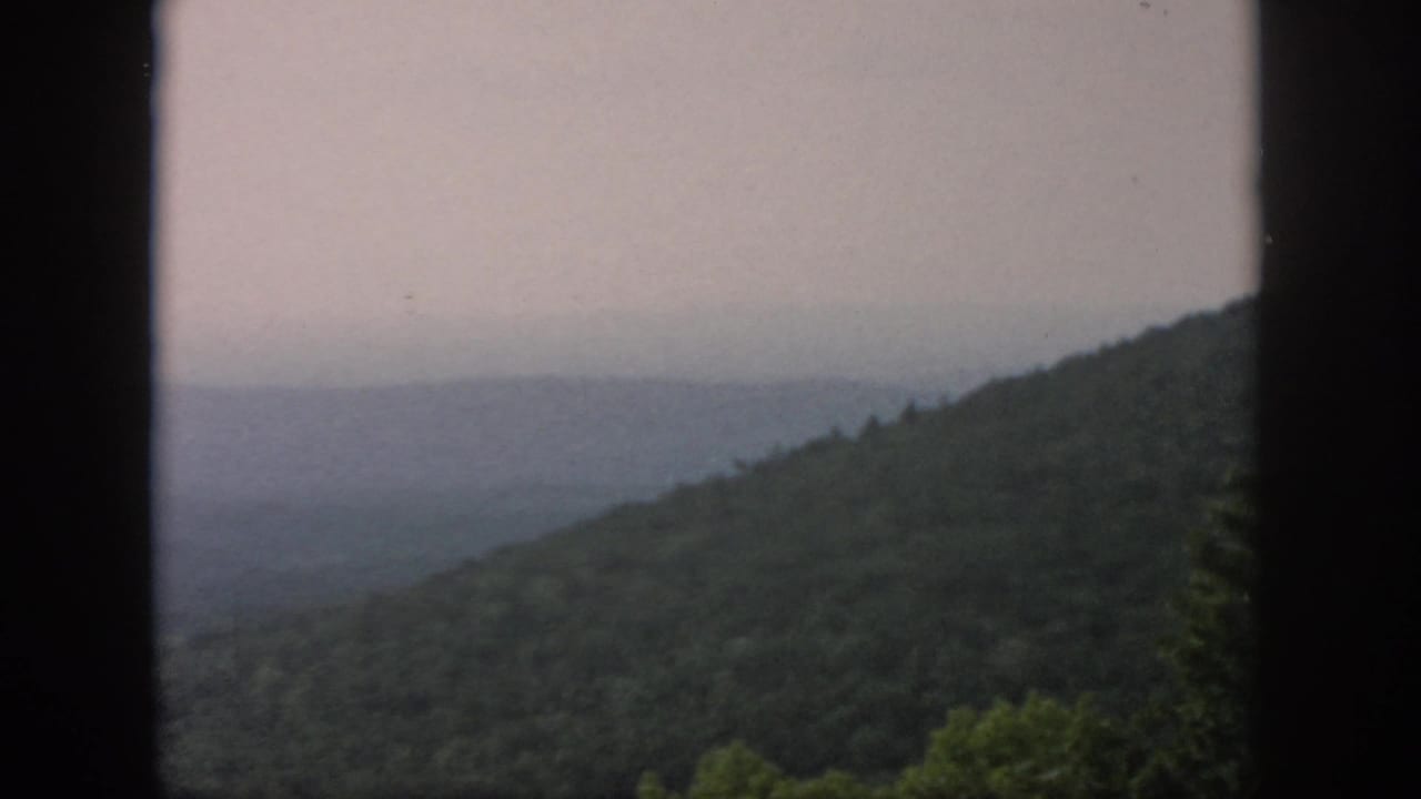 1958 Dayton, Ohio metadata supports this hazy wooded valley view framed by dark vertical window edges on 8mm film.