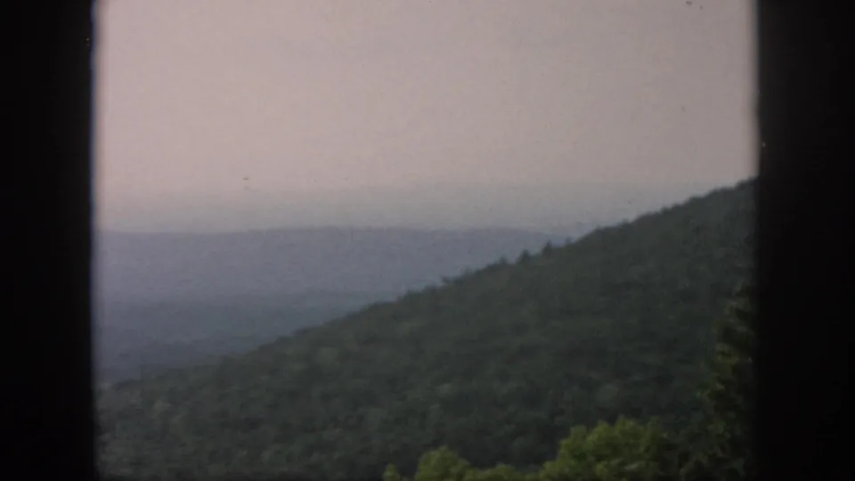 1958 Dayton, Ohio metadata supports this hazy wooded valley view framed by dark vertical window edges on 8mm film.