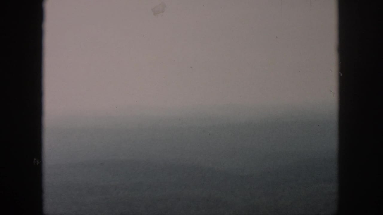 1958 home-movie frame attributed to Dayton, Ohio, showing a fog-softened aerial view through aircraft window bars.