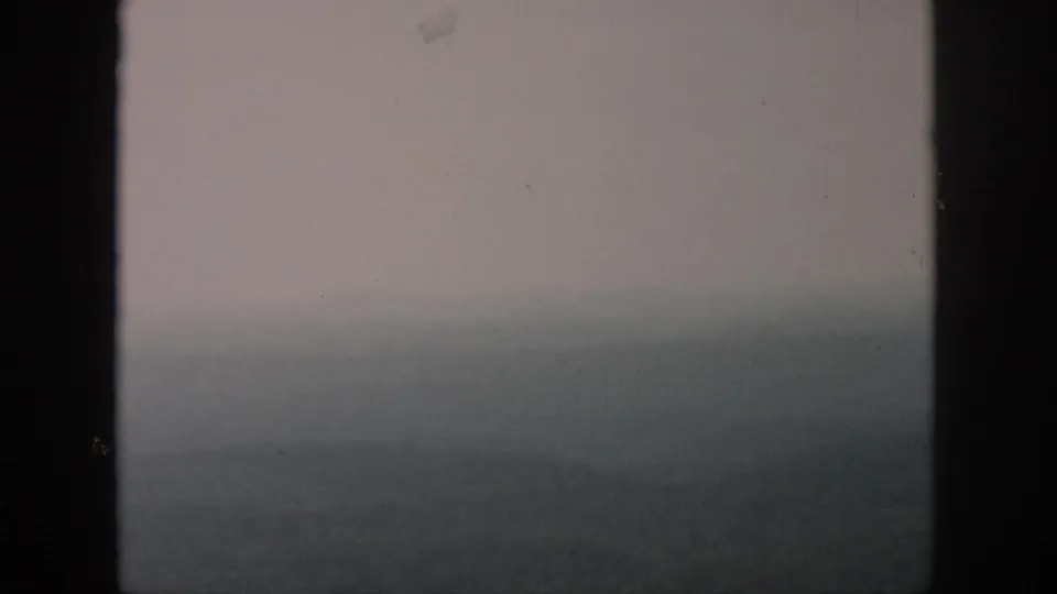1958 home-movie frame attributed to Dayton, Ohio, showing a fog-softened aerial view through aircraft window bars.