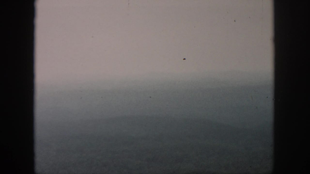 Muted aerial view of hazy forested hills framed by dark vertical window bars.
